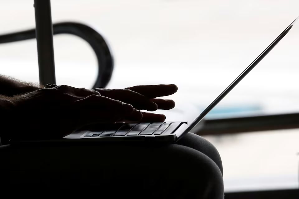 Silhouetted hands typing on a laptop against a bright window.